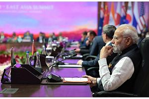 Au premier plan de la photo, on voit Modi, le premier ministre indien, assis devant un micro. Derrière lui, on devine d'autres dirigeants nationaux. Au dernier plan de la photo, on devine des drapeaux de différents pays, avec un fond d'écran rose qui tire vers le violet.