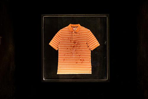 Sur un fond noir, ressort un t-shirt orange maculé de tâches.